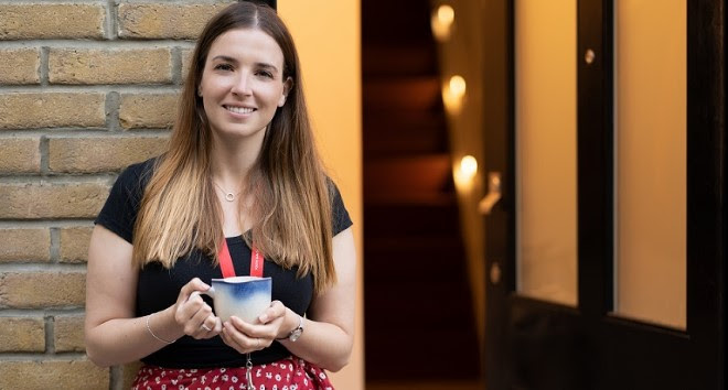 Jenny, our Operations Manager stood holding a cup of tea outside an open door