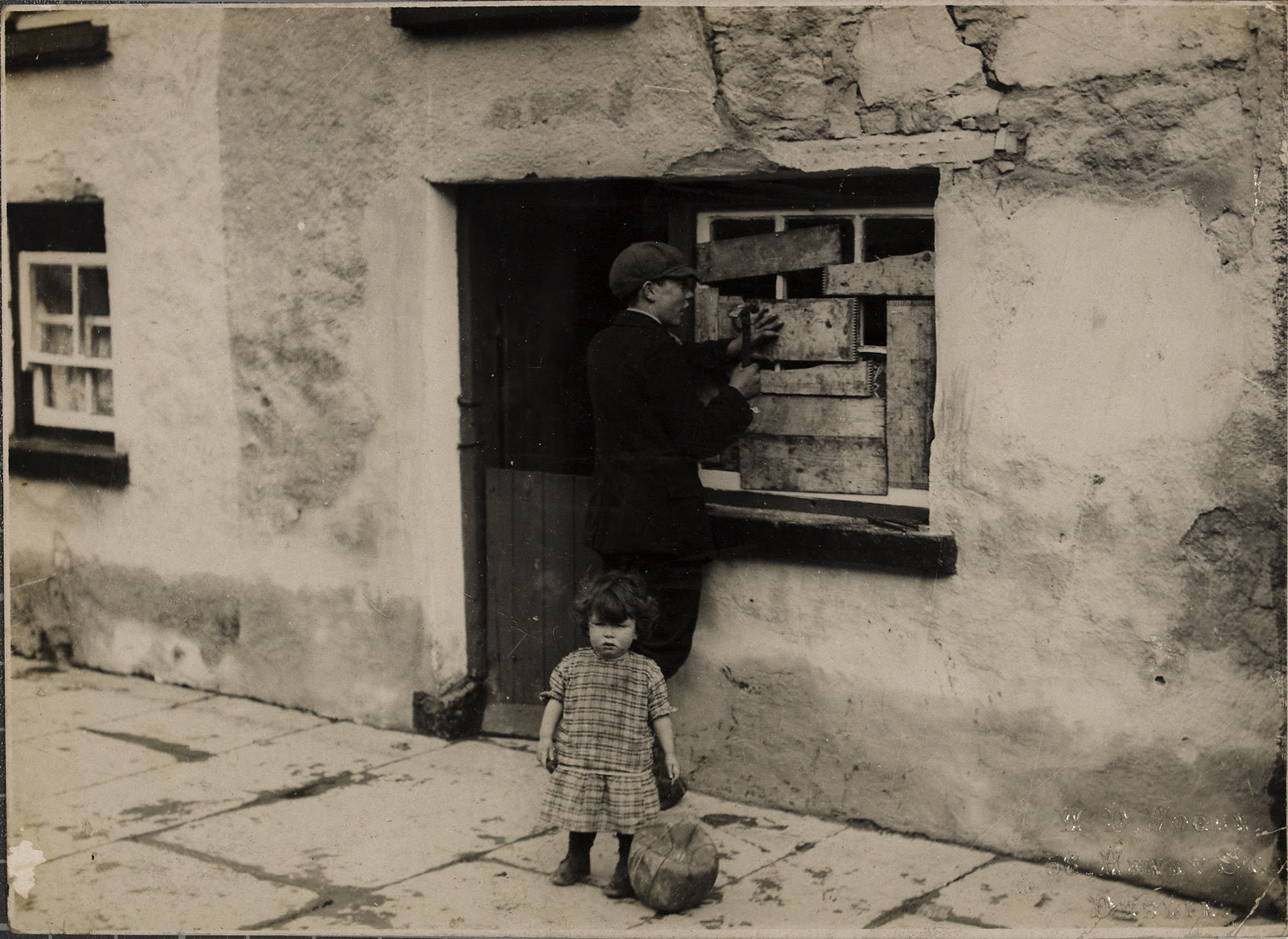 House in Templemore in aftermath of raid by Tans - boy boarding up window and child with a small ball | by National Library of Ireland on The Commons