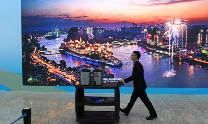 A worker pushes a cart past a screen showing a photo of the Fujian Pilot Free Trade Zone, at the venue of the Belt and Road Forum in Beijing on April 26, 2019. (Greg Baker/AFP via Getty Images)
