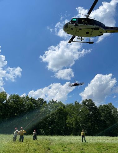 workers in a field hoisting up a rescue basket into a helicopter