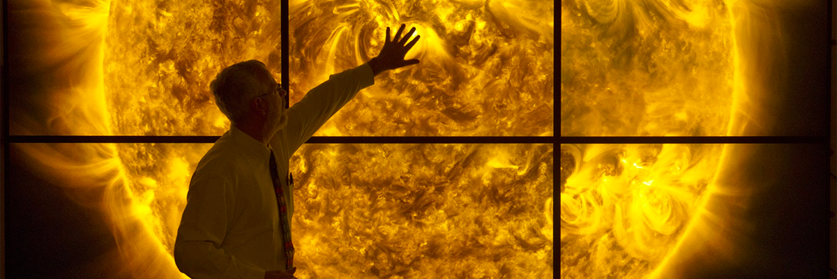 A photograph of an educator in front of a large video display of the sun's surface.