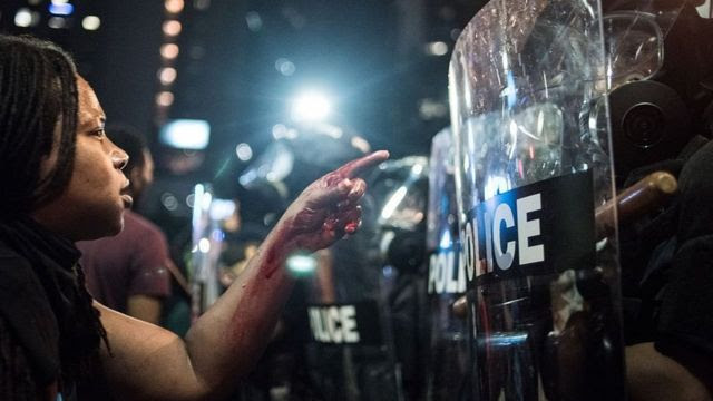 Manifestante do Black Lives Matter na frente de uma linha de policiais de choque