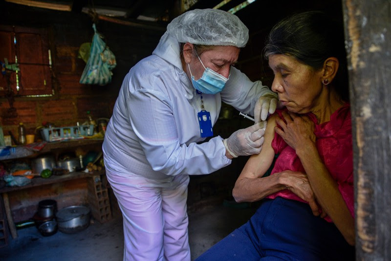 A healthcare worker administers a dose of COVID-19 vaccine to an elderly woman in her home in rural Colombia