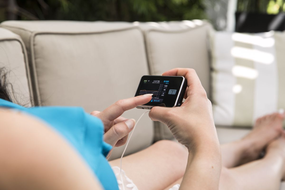 Close-up of woman holding an insulin pump while laying on outdoor couch.