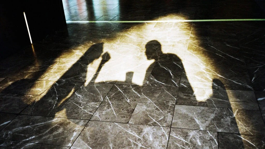 The shadow of two people sat at a table drinking and eating