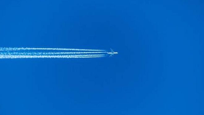 Avião voando e fazendo rastro de fumaça branca no céu