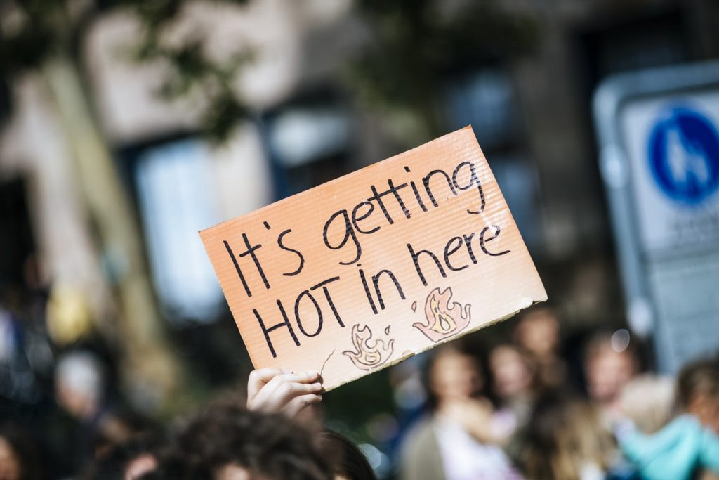 a protestor holds a cardboard sign reading 'it's getting hot in here!'