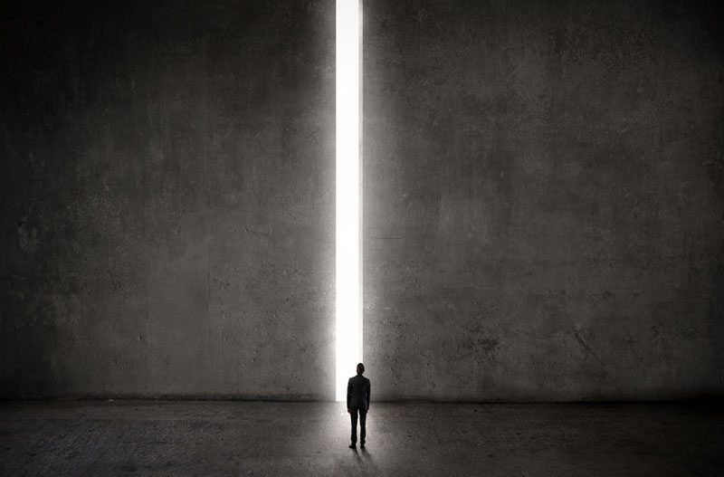 Ein Mann steht in einer leeren Halle vor einer Wand. Nur ein Spalt ist geöffnet, durch den Licht hereinscheint. Foto: olly - fotolia.com