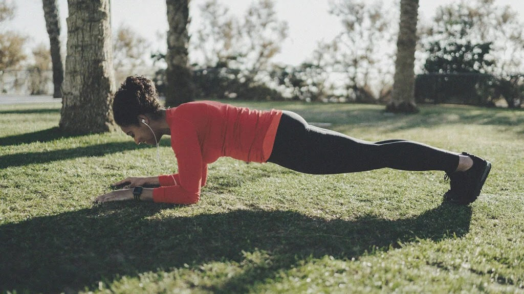 a woman performs one of the core exercises known as the plank in a public park