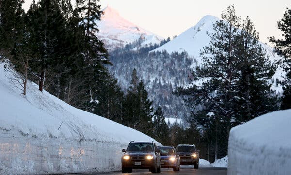 Three
                              vehicles on a mountain road, with snow
                              next to them piled higher than their
                              roofs.