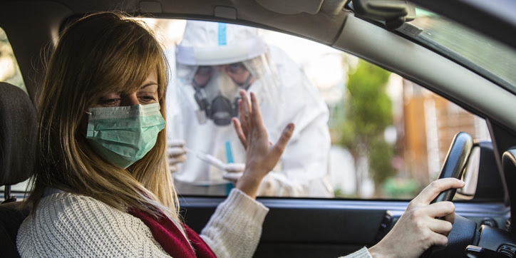 A white woman in a car refuses treatment from a medical professional in PPE outside her window.
