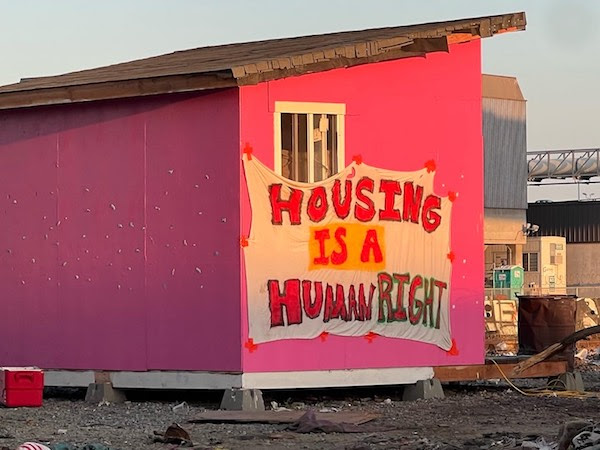 Photo of pink Wood Street tiny home that was recently demolished that has a banner on it that reads “Housing as a Human Right”