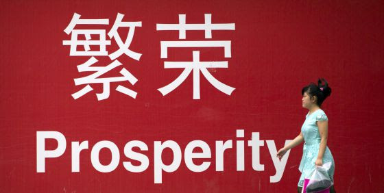 Una mujer camina junto a un cartel en el que se lee la palabra prosperidad en chino e inglés, en Pekín