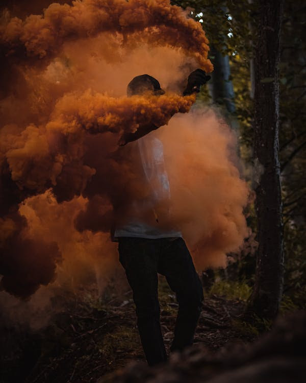 Man in Black Jacket Standing in Front of Orange Smoke