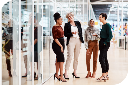 A group of women in an office environment have a friendly conversation.