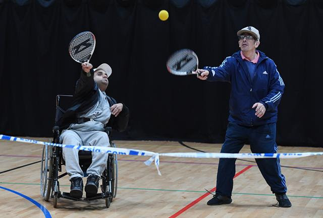 Two men, one a wheelchair user, playing tennis in an indoor sports hall