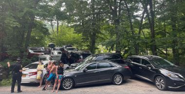 a bunch of cars parked illegally blocking other cars in the enterance to the park
