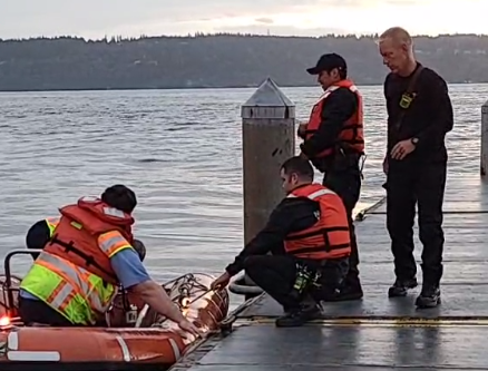 Two people in rescue boat at dock talking to three people standing on the dock