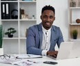 black young man in suit in office with laptop