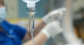 close up shot of an infusion bag with nurse in background preparing to infuse a patient