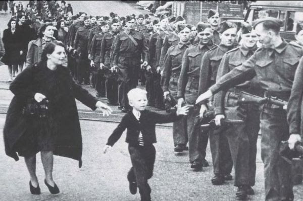 Boy reaches for his father's hand as he marches in a line of soldiers.