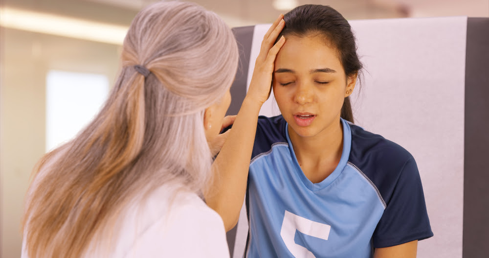 female doctor examines female teenage soccer player with a headache
