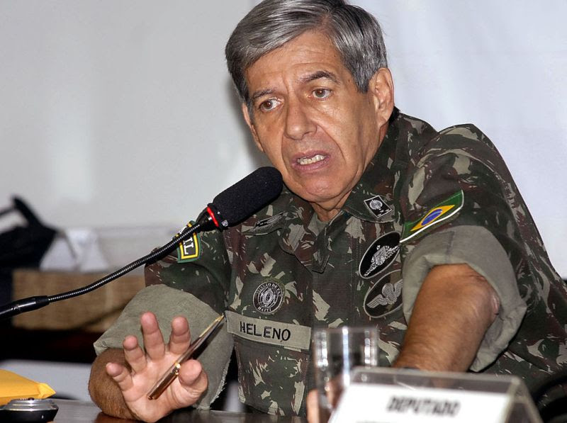 Augusto Heleno é um homem na faixa dos 60 anos, branco e com cabelos grisalhos. Eles teve uniforme militar e fala ao microfone, sentado em uma mesa