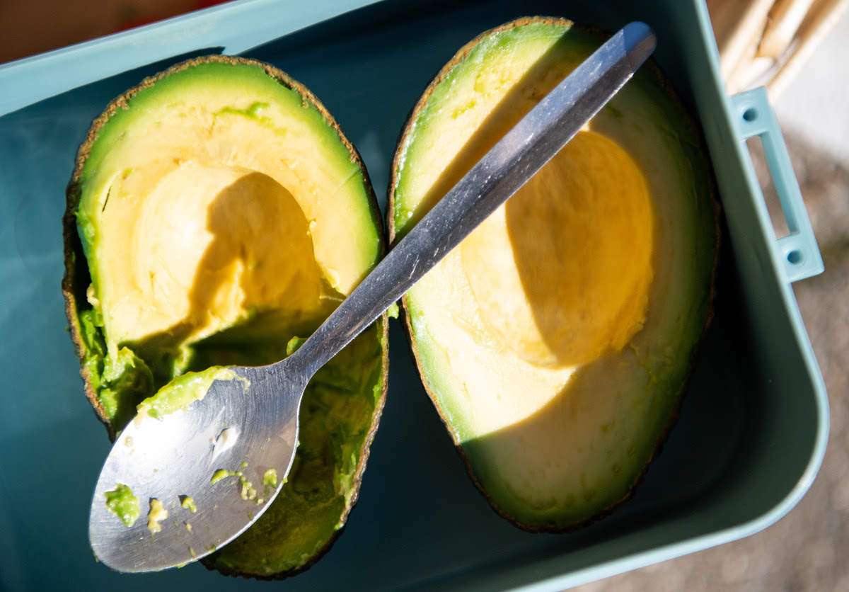 A spoon lies over a sliced avocado.