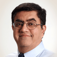 Dr. Chopra, a man with short black hair and glasses. He wears a white shirt and a tie