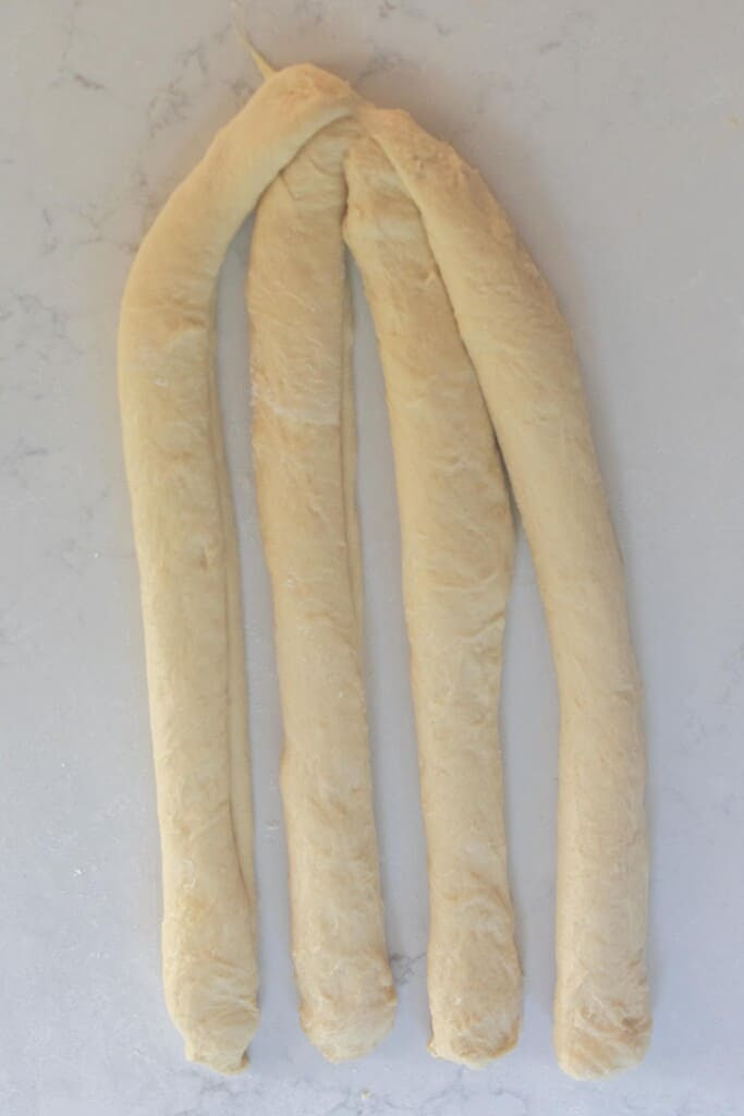 braiding 4 strands of sourdough challah dough  on a white countertop 