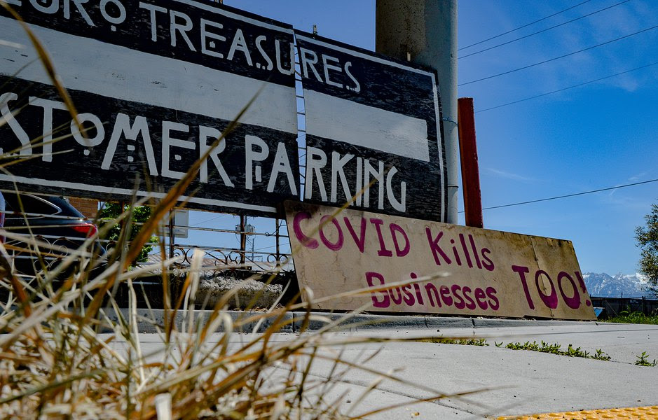 An empty parking lot with a sign that reads about the virus killing businesses too.