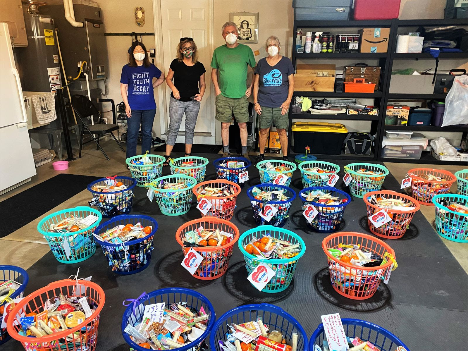 Picture of 4 people standing behind 25 plastic baskets filled with goodies.