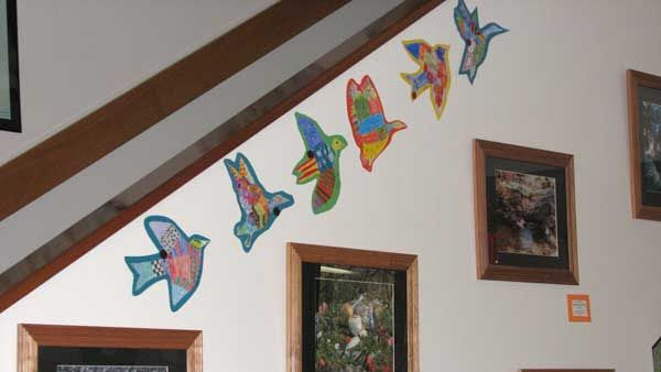 Several bird shaped of colorful paper appear to fly up along a stairwell wall. Several photos of nature scenes are below.