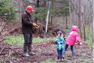 A man watches two small children as they walk through the woods