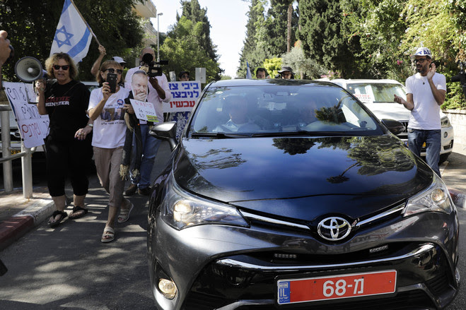 Israeli protesters hold banners as police arrive at the prime minister’s residence in Jerusalem to... Israeli protesters hold banners as police arrive at the prime minister’s residence in Jerusalem to question Mr. Netanyahu on Aug. 17.