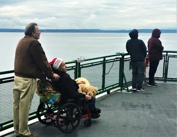 Three people standing and one in a wheelchair wearing a Santa hat on the outdoor deck of a ferry