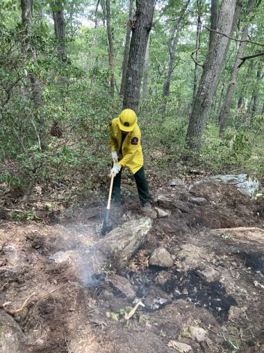 Forest Ranger dressed in yellow fire gear helps extinguish wildfire