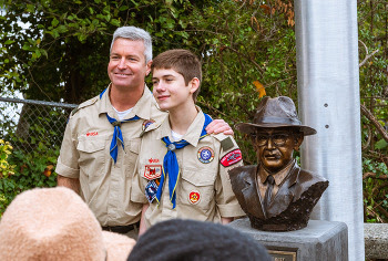 Two people in boy scout uniforms standing next to a bust of a person