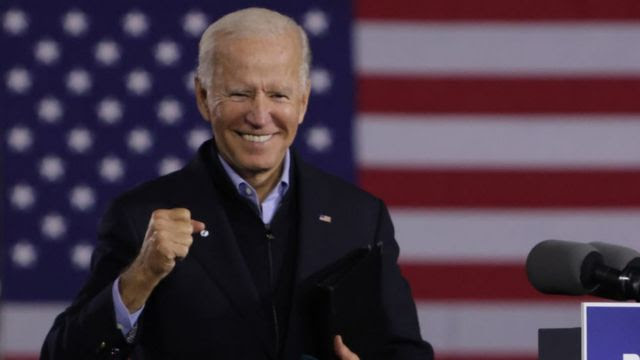 Biden faz gesto de vitória em frente a bandeira dos EUA projetada ao fundo