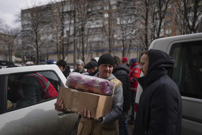 A person carries a box and a wrapped blanket as humanitarian aid is distributed in Mariupol. 