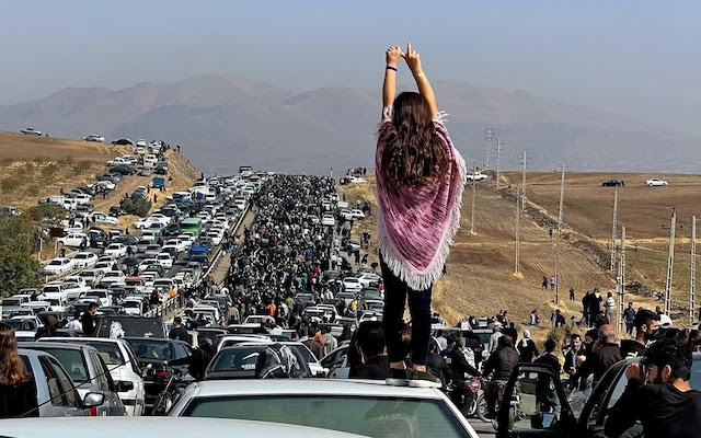 An unveiled woman standing on top of a vehicle as thousands make their way towards a cemetery in Mahsa Amini's home town in the western Iranian province of Kurdistan