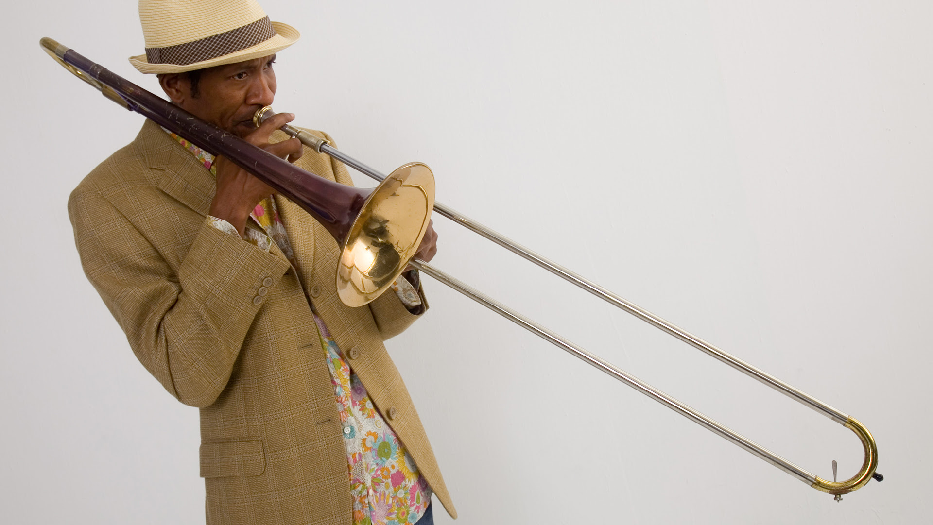 A man wearing a straw hat and linen jacket playing the trombone