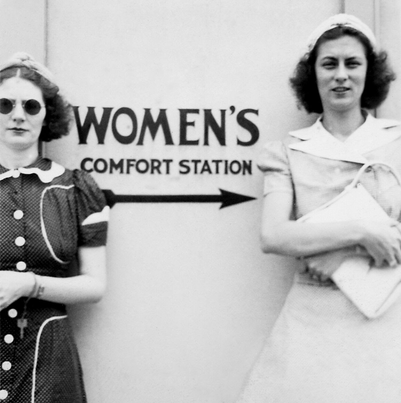 Two young women stand by a restroom sign, ca. 1939.
